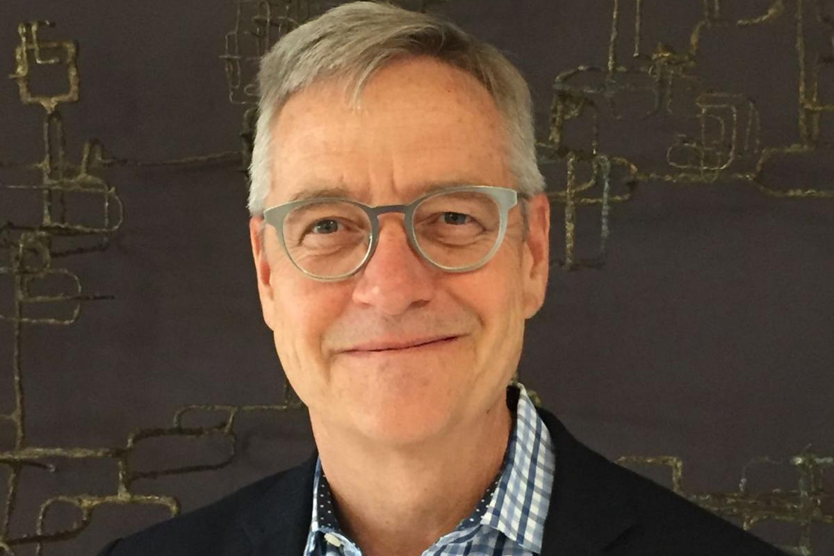 Color portrait of the head and shoulders of Tom Mayes, wearing glasses, a checkered shirt, and a dark gray sportscoat