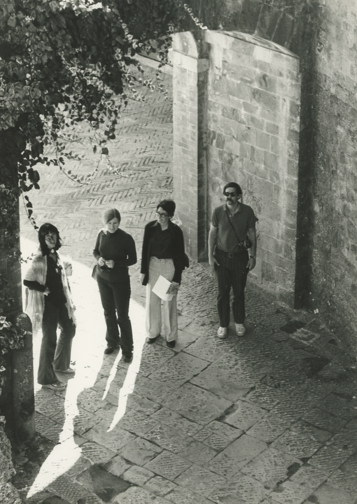 Black and white photo of four light skinned people standing in a building entrance, as seen from the second floor