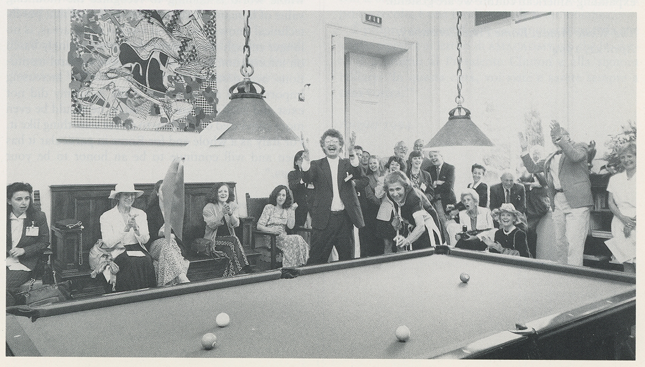 Black and white photograph from 1994 of many light skinned people clapping and cheering on a woman shooting pool in a salon