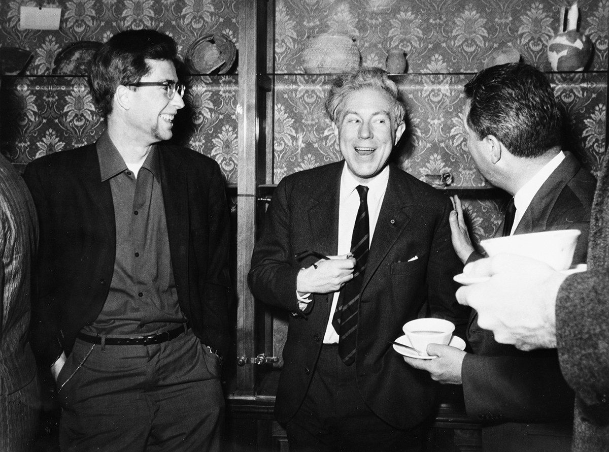 Black and white photo from 1966 showing three men talking to each other at an indoor reception at a conference