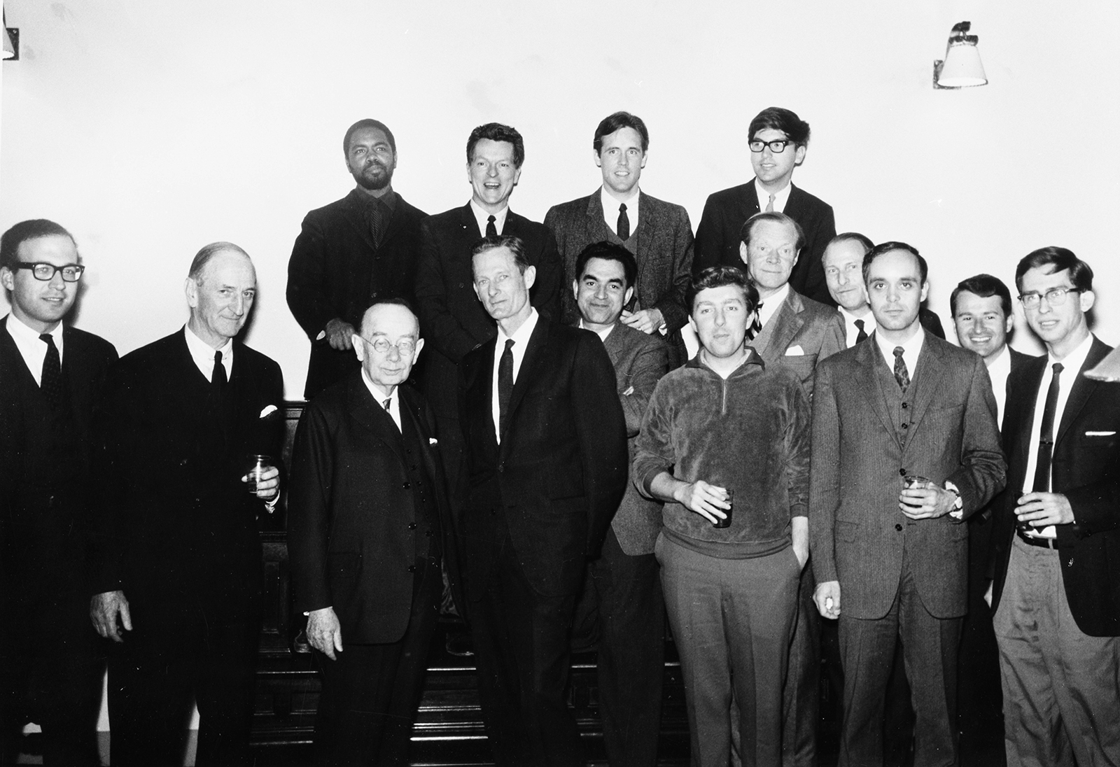 Black and white group portrait of fifteen men of various races; most of them wearing dark suits and looking at the camera