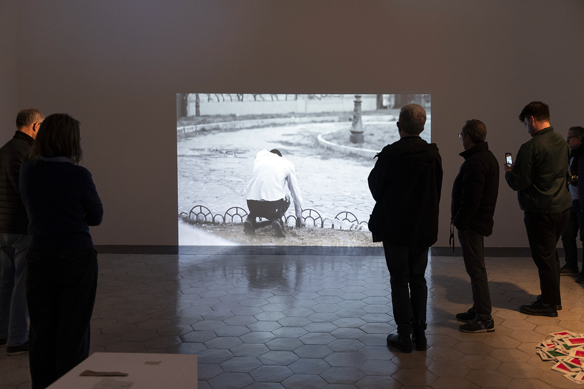 Color photograph of several people standing in a darkened gallery looking at a video projection on the wall