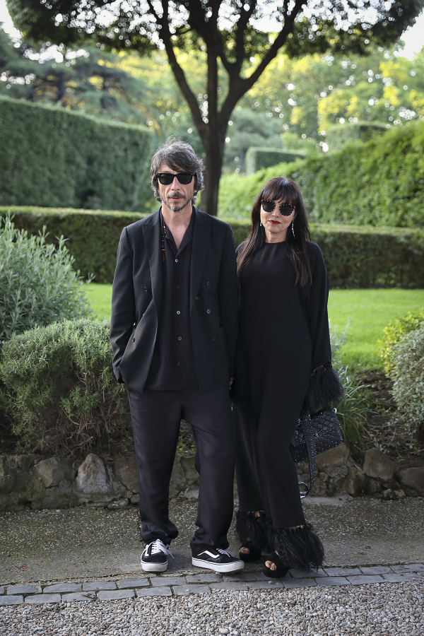 color photo of a man and women wearing black and sunglasses standing in a garden