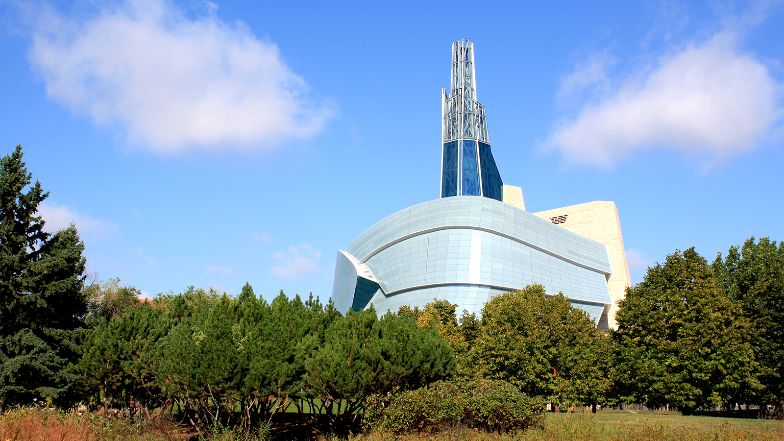 Color photograph of a building complex in a modern style, in front of a green garden or natural setting