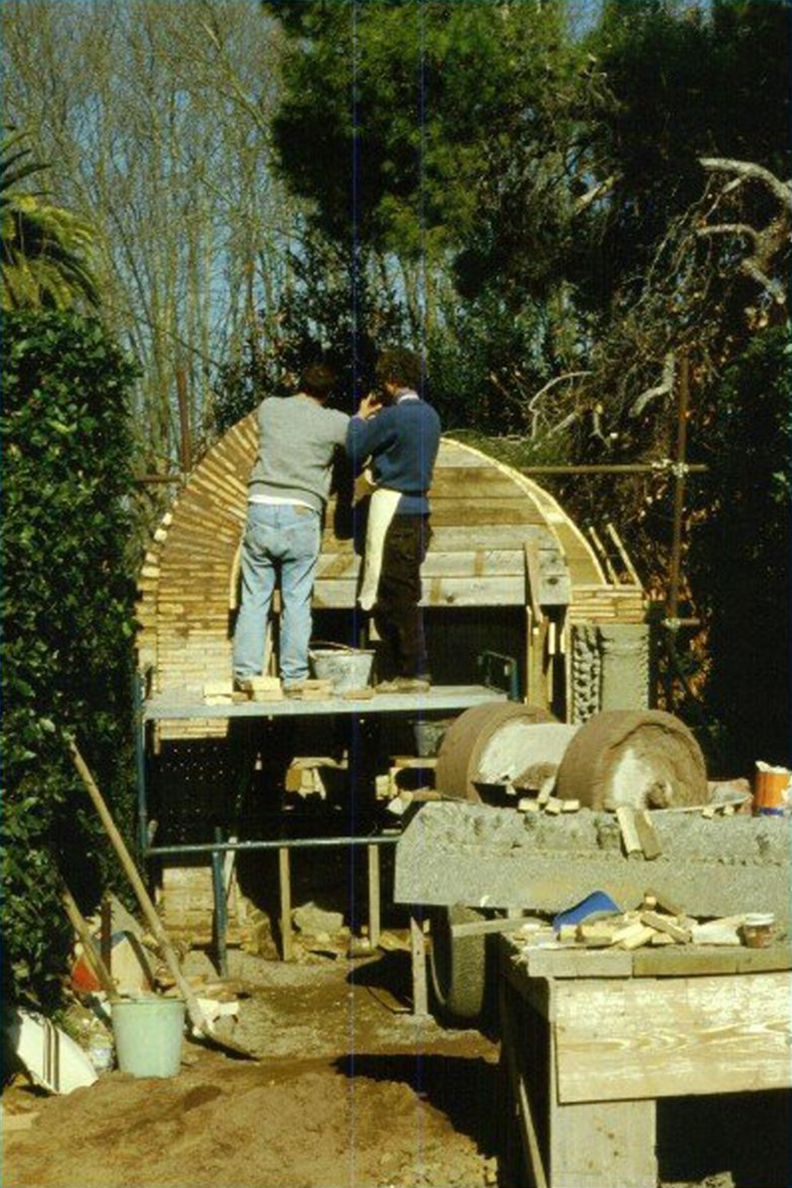 Color photo of two men building an arched structure in a green garden