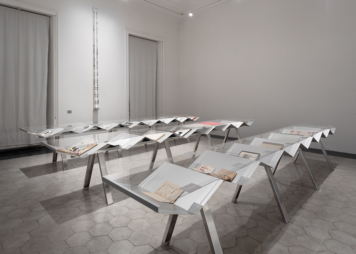 color photo of a white walled gallery with three jagged tables holding artist's books