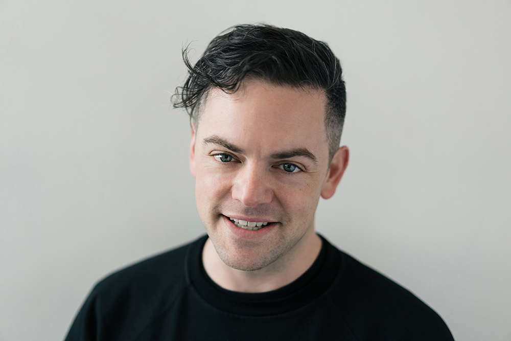 Color photograph of the head and shoulders of Nico Muhly, smiling and looking at the camera