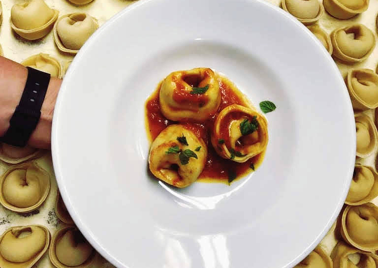 Color photograph of tortellini with tomato sauce on a white plate