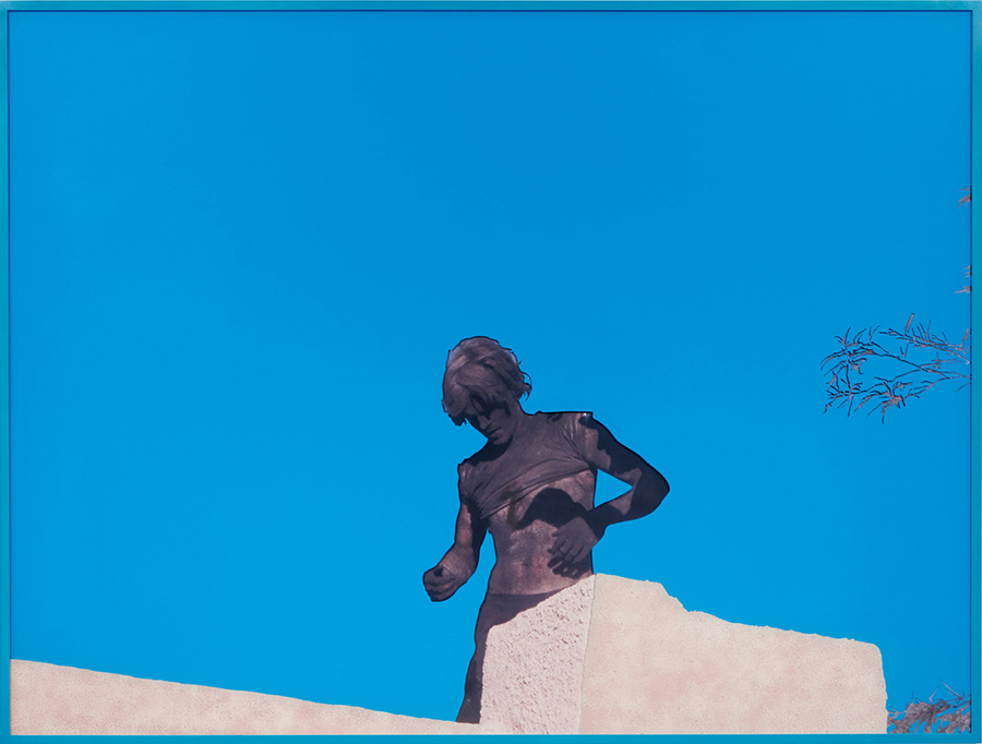 Color photograph of a man covered in black soot standing on a rooftop underneath a striking clear blue sky