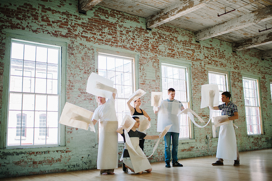 dancers with paper props in a brick walled room