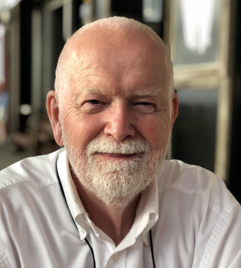 Color photograph of the face of an older light skinned man about 60 to 70 years old, smiling and looking straight at the camera