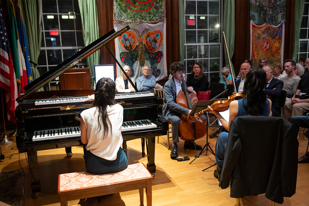 Color photo of a piano trio playing music for a small indoor audience