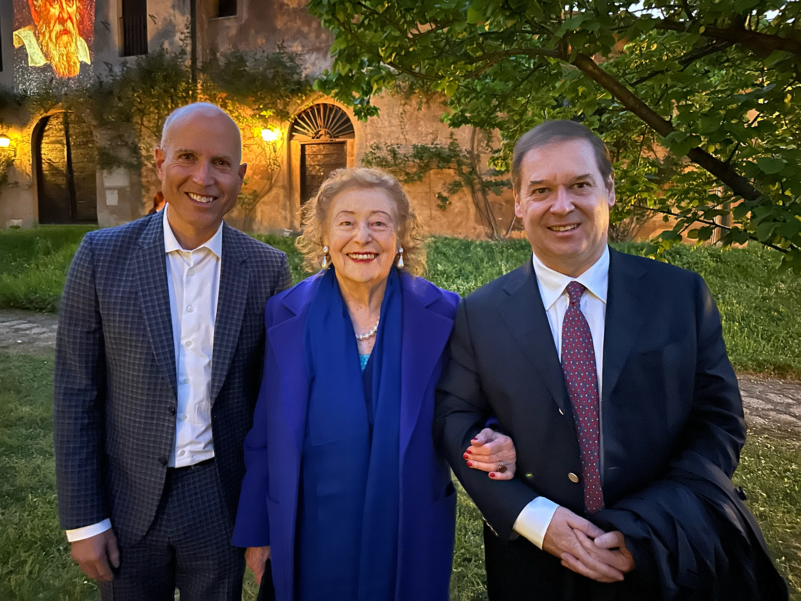 color photo of two men and one elderly woman smiling at the camera in a garden location