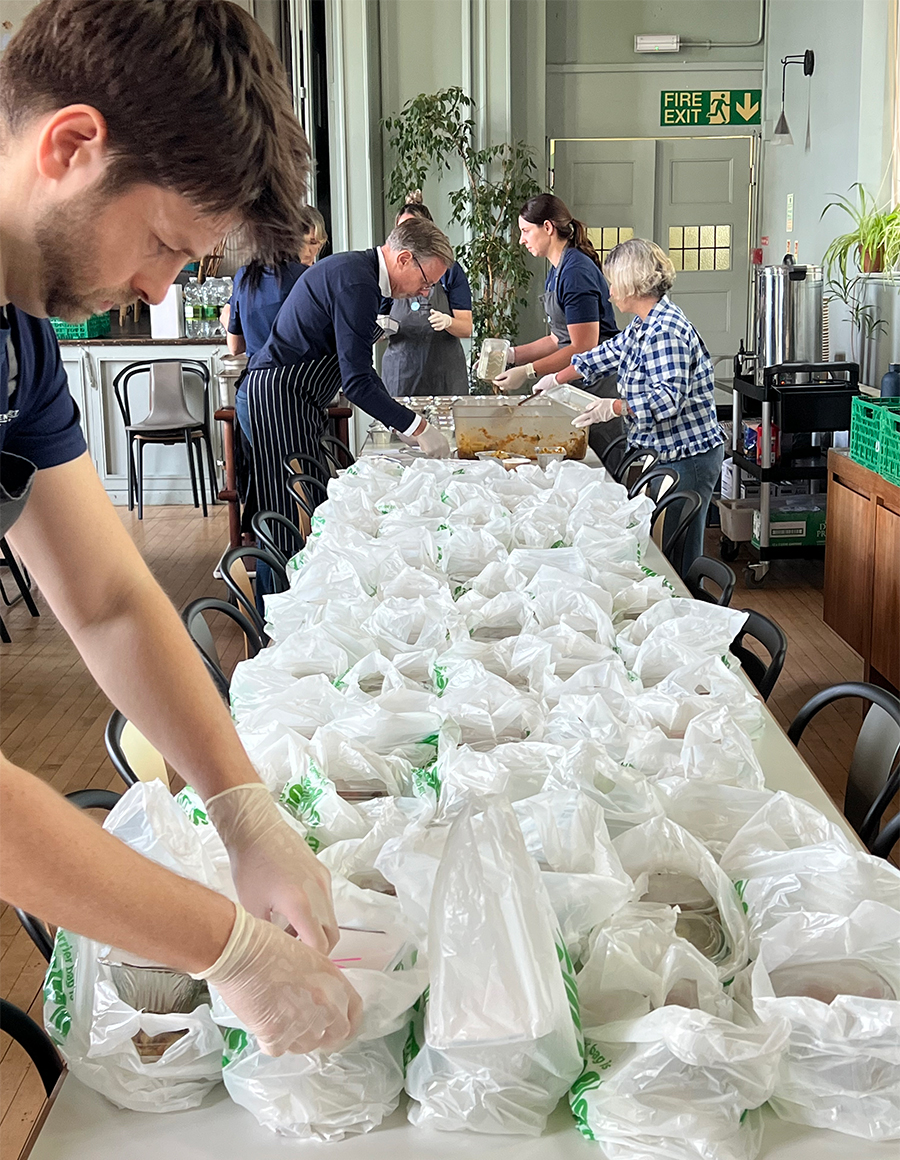Color photo of kitchen staff placing packaged meals in white plastic bags