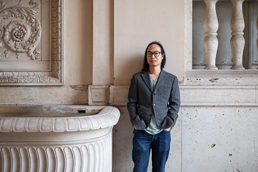 Color photograph of an Asian man standing next to a marble fountain basin
