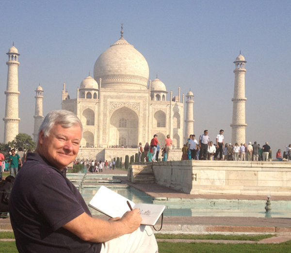 Color photograph of a man with a sketchpad drawing the Taj Mahal in India, seen in the distance