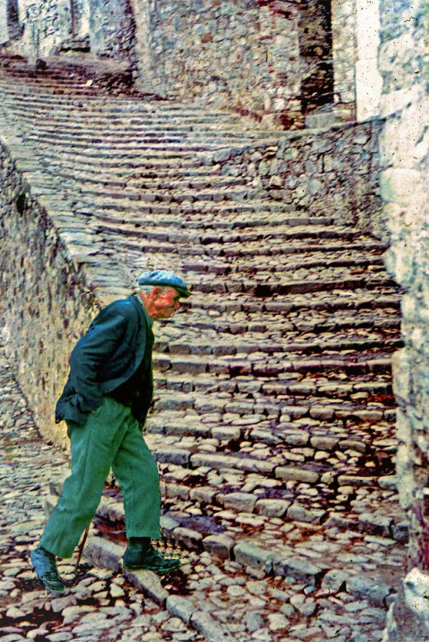 Color photograph of an elderly Italian man stepping forward to climb a flight of outdoor stone stairs