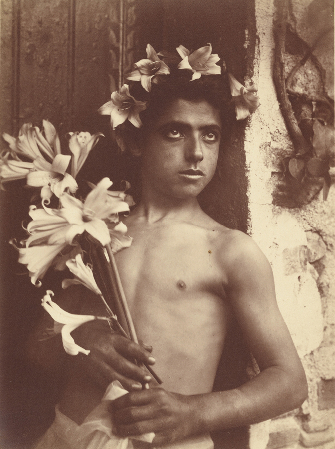 Monochromatic brown 19th-century photograph of the head of a young boy wearing a floral crown and staring off camera