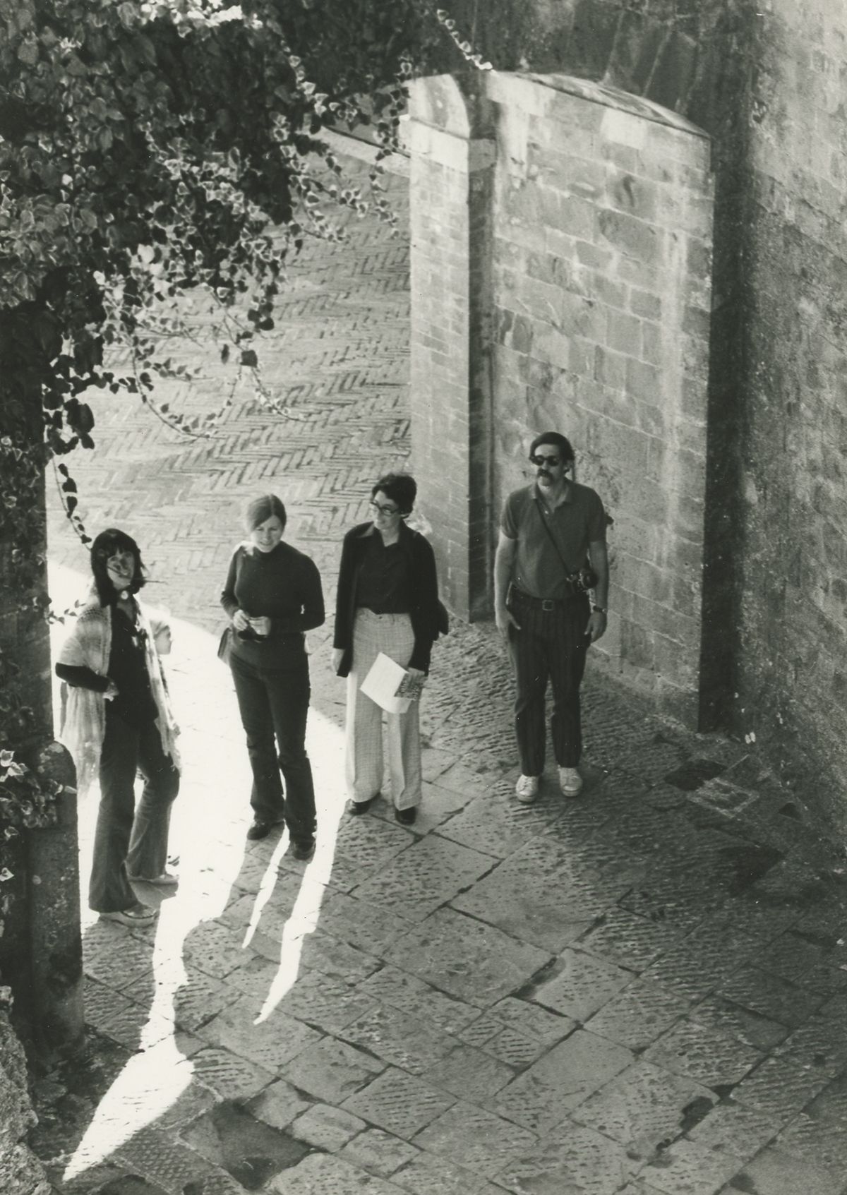 Black and white photo of four light skinned people standing in a building entrance, as seen from the second floor