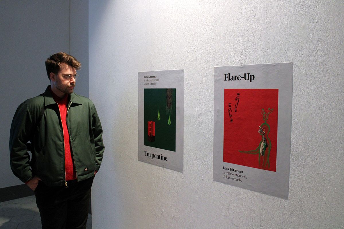 A man looking at two prints that mimic book covers that adhere to a white gallery wall
