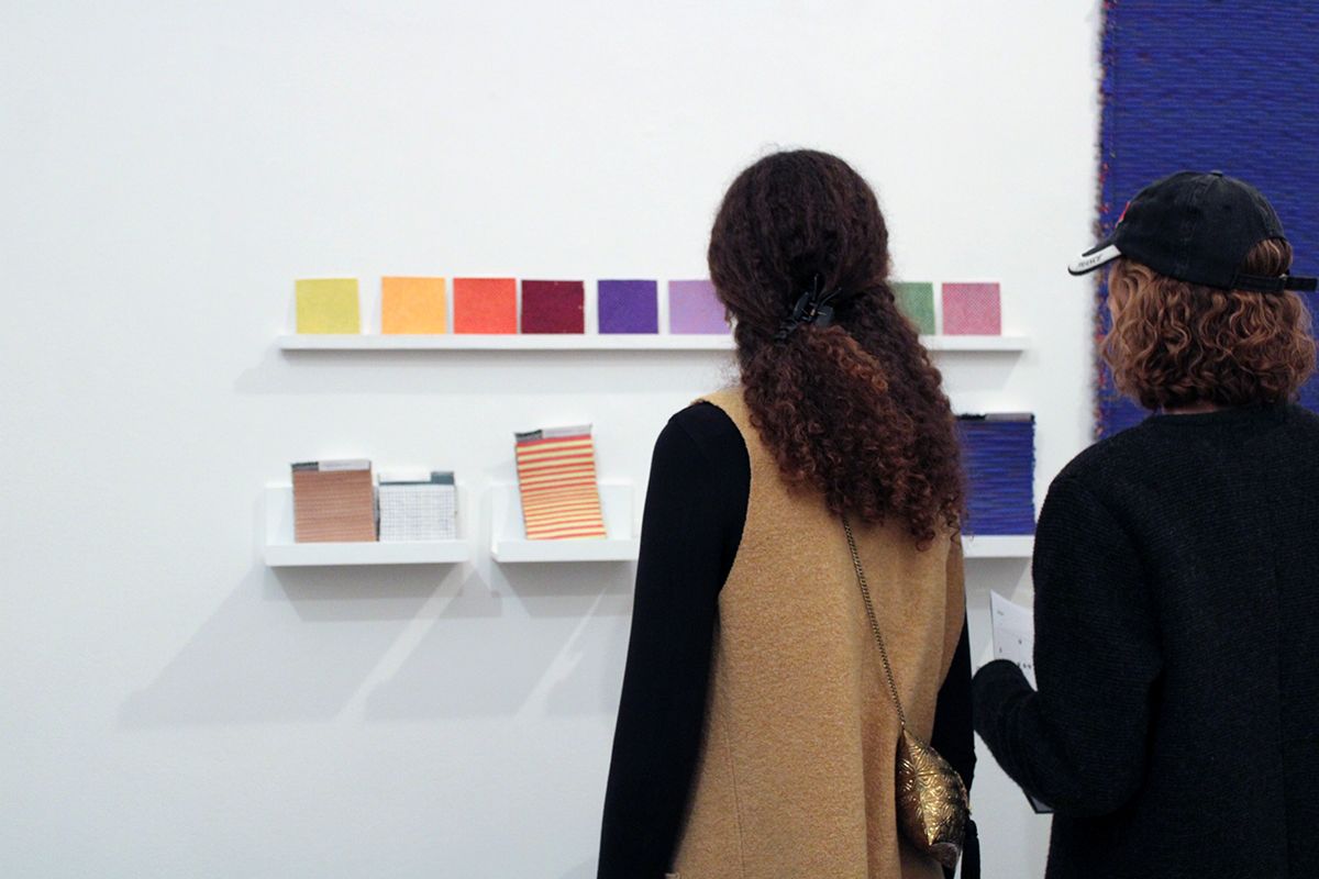 Color photograph of the backs of two people looking at fabric swatches in an artist's studio