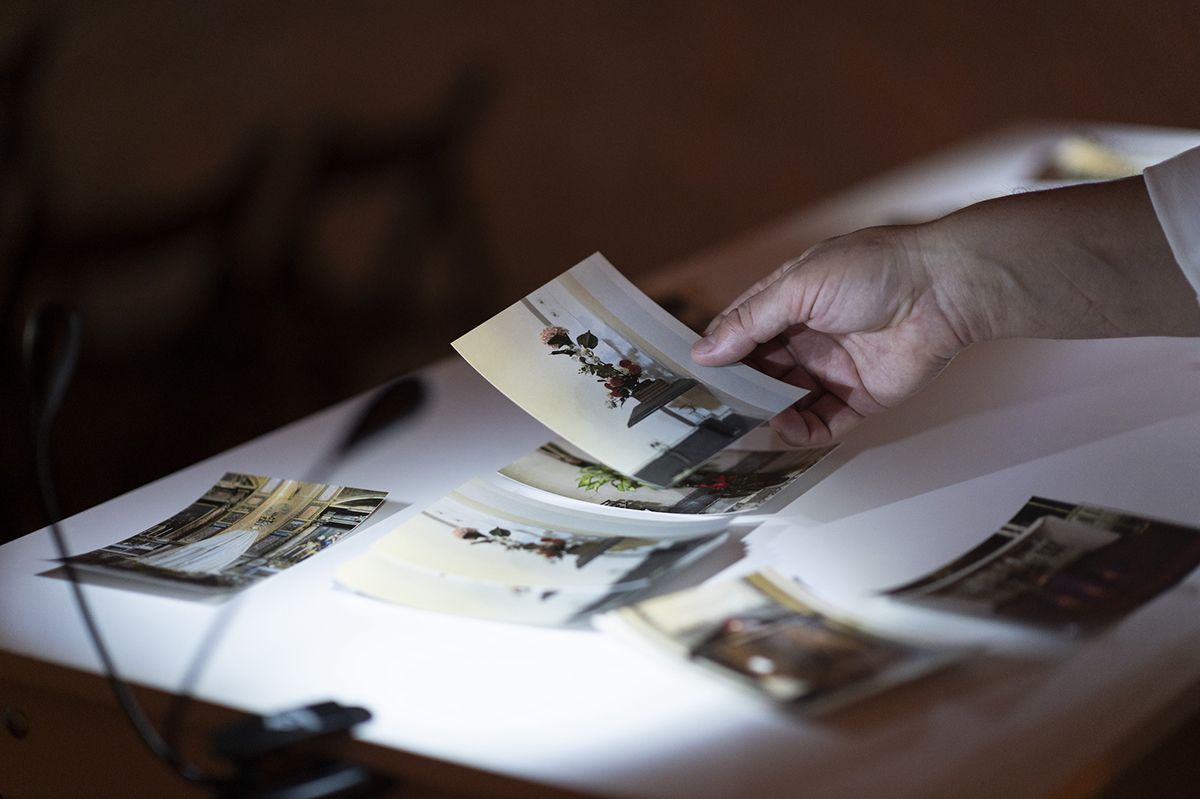 Color photo of a hand picking up a printed photo from among a group of photos resting on a table