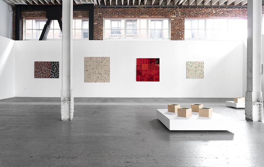 Color photograph depicting the installation of several ceramic tile artworks on the walls and floor of an art gallery 