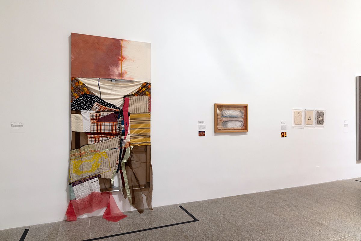Color photo of an exhibition installation with one large and two small artworks on a white wall