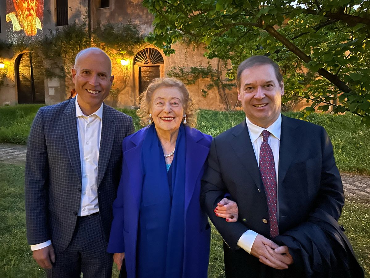 color photo of two men and one elderly woman smiling at the camera in a garden location
