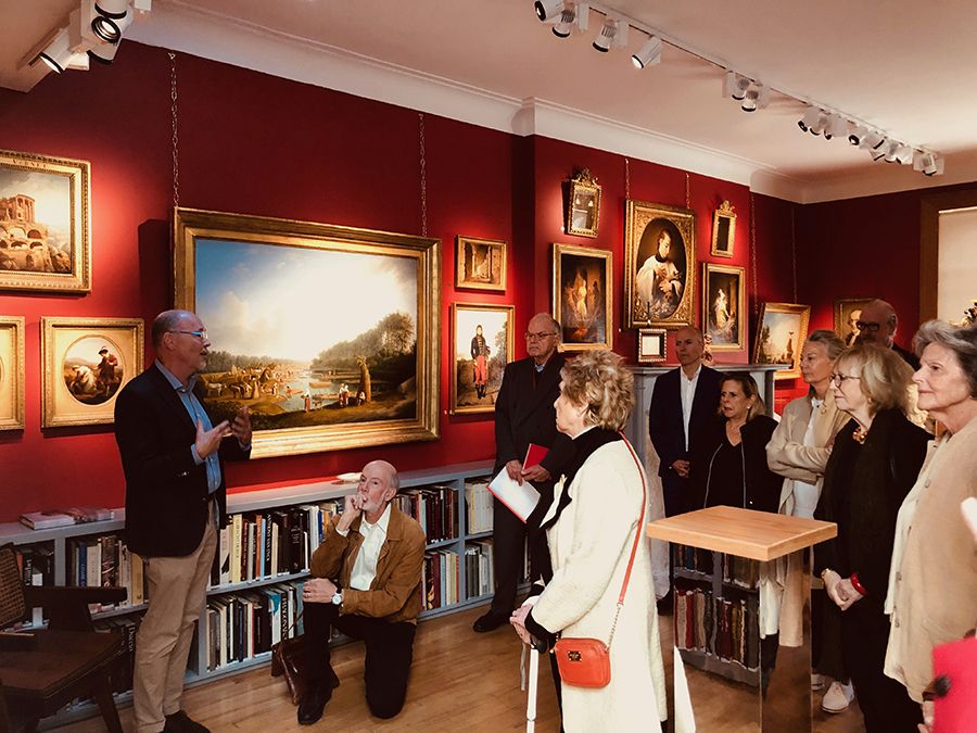 Color photograph of a man leading a tour of about ten people in a gallery with various paintings hanging from red walls