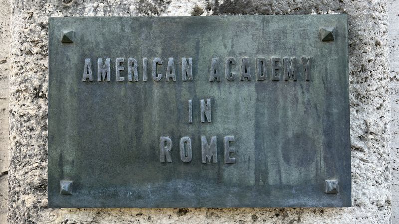 Color photograph of a oxidized steel nameplate on a stone wall; the sign reads American Academy in Rome