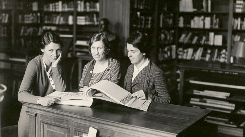 Black and white photo of three light skinned women in a library in 1933