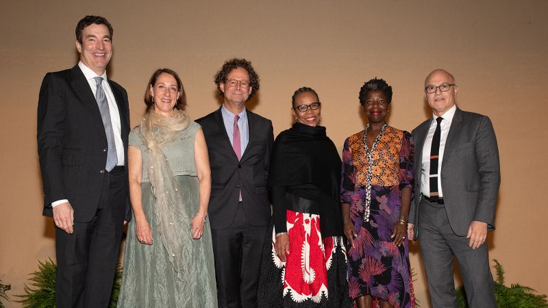 Color photograph of six people (two dark skinned and four light skinned) standing in a row wearing festive gala attire