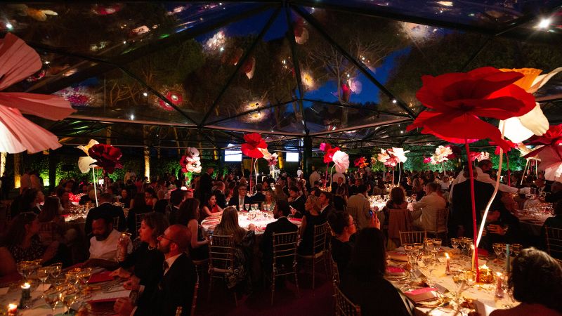 Color photograph of a gala dinner tent at night, with people sitting at round tables