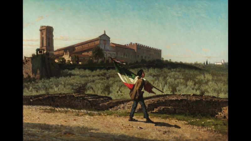 Color reproduction of a 19th-century oil painting depicting a young man walking along a path carrying an Italian flag and pole on his shoulder; on a hill in the field behind him are several multistory buildings that look a couple hundred years old