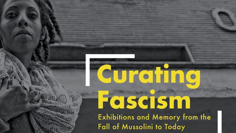 Detail of a book cover with the title (Curating Fascism: Exhibitions and Memory from the Fall of Mussolini to Today) in yellow letters superimposed over a black and white photograph, that depicts a dark skinned with dreadlocks looking down at the camera