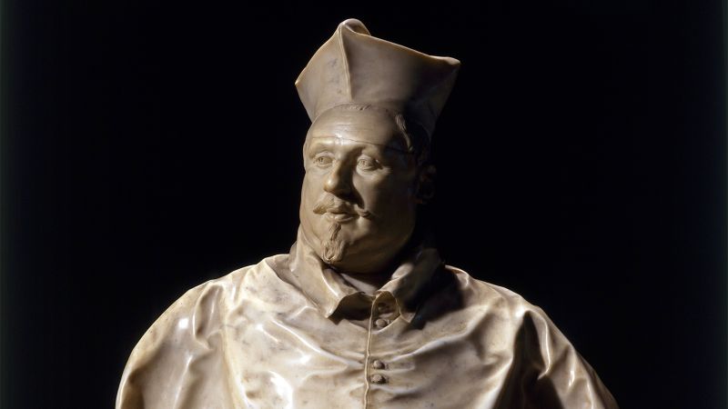 Color photo of an ornate sixteenth-century bust of a man in carved stone set against a black background
