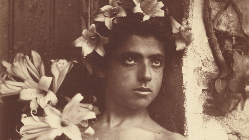 Monochromatic brown 19th-century photograph of the head of a young boy wearing a floral crown and staring off camera