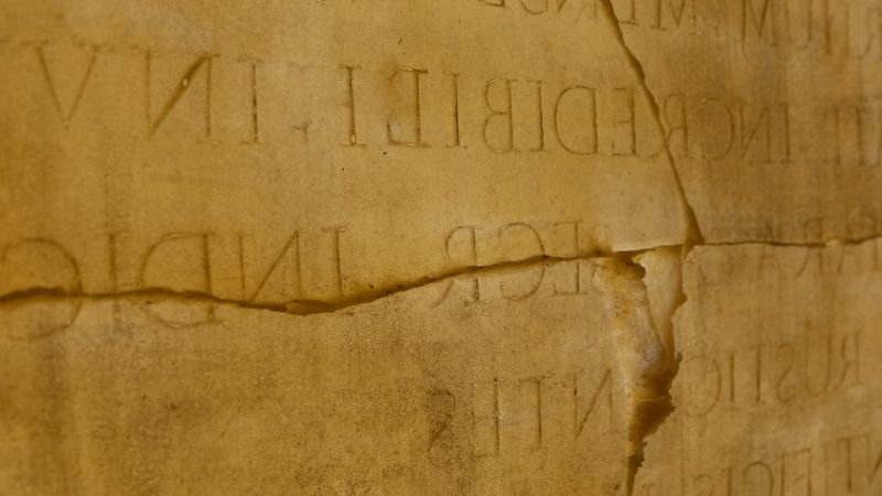 Color photo of a detail of an artwork consisting of a latex mold of a ancient Roman epigraphic stone, with backward Latin letters on stone