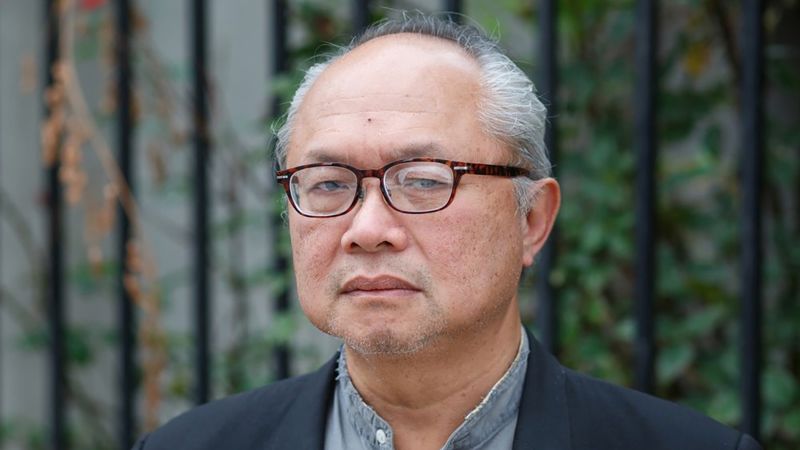 Color photograph of an older Asian man wearing glasses