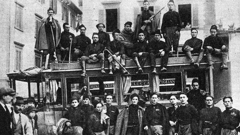 Grainy back and white photograph from the 1920s of about thirty Italian men wearing Fascist uniforms and posing in front of and on top of a bus