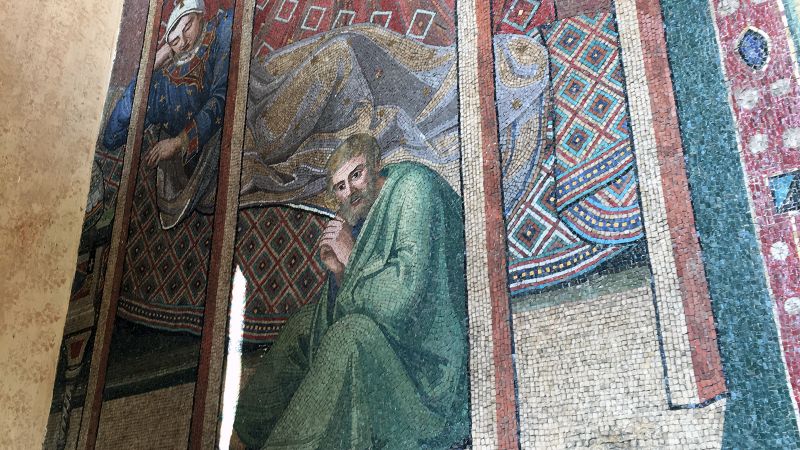 Color photograph, taken at an oblique angle, of a mosaic on the façade of Santa Maria Maggiore, showing a man with his eyes closed and another man with his eyes open