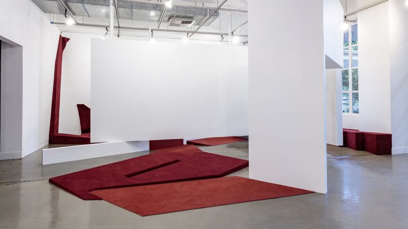 Color photographs of an architectural installation of temporary white walls and low, angled red-carpet-covered platforms and ramps