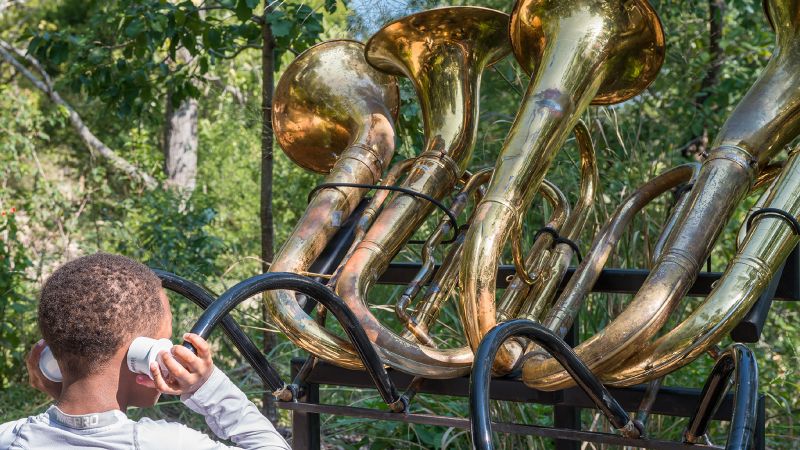 Color photograph of a boy listening to a sculptural creation made of repurposed tubas