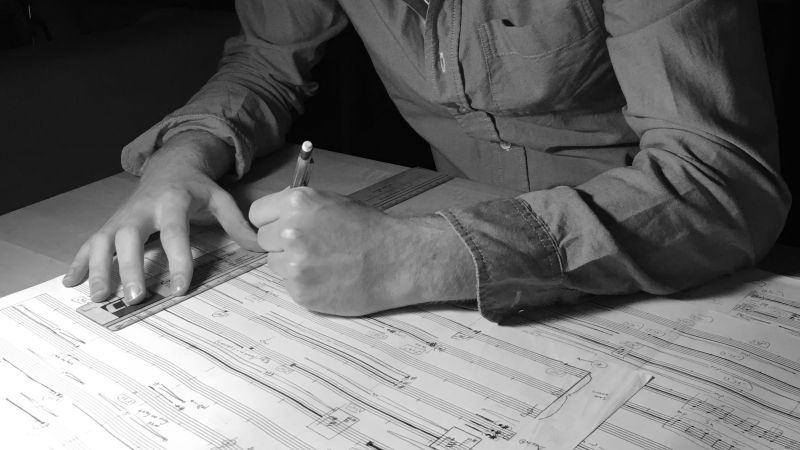 Black and white photograph of William Dougherty's arms and hands as he writes notation on a musical score sheet