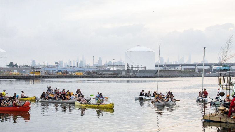 Color photo of a couple dozen people in small boats on an urban river
