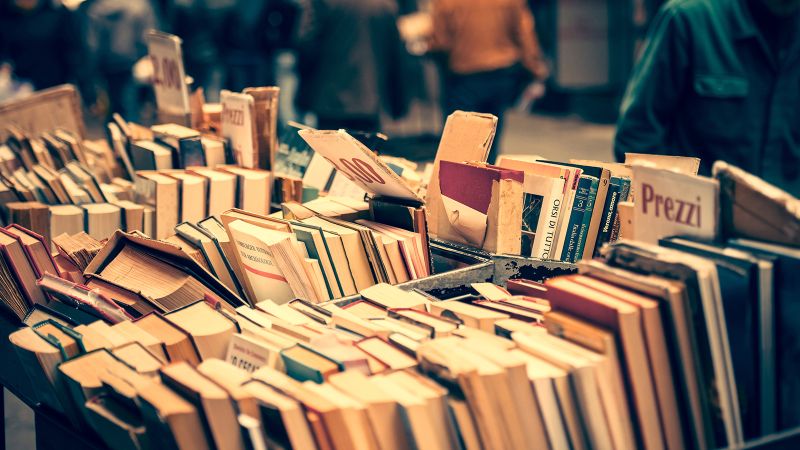Color photograph of a street book stall in Milan, with dozens of books lining a wooden open topped shelf