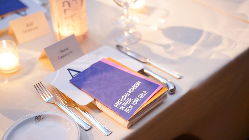 Color photograph of a place setting at a dining table, with a printed event program resting on the plate
