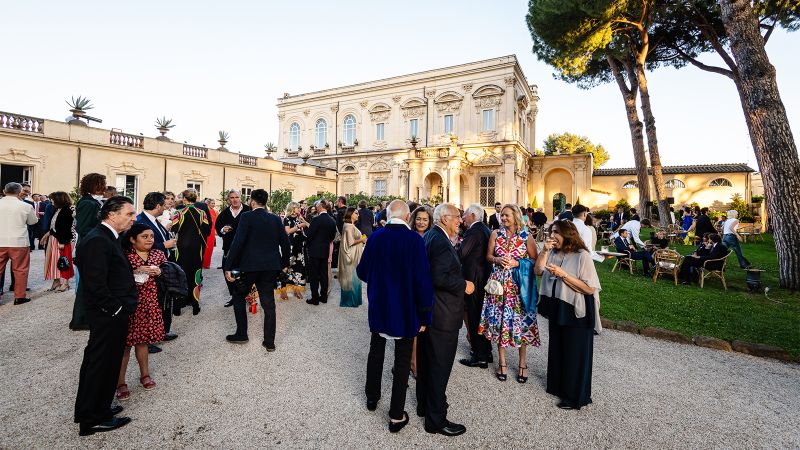 Color photograph of dozens of people standing and talking with cocktails