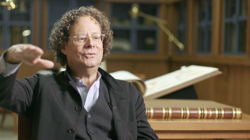 Color video still of a light skinned man being interviewed on camera in a rare book library
